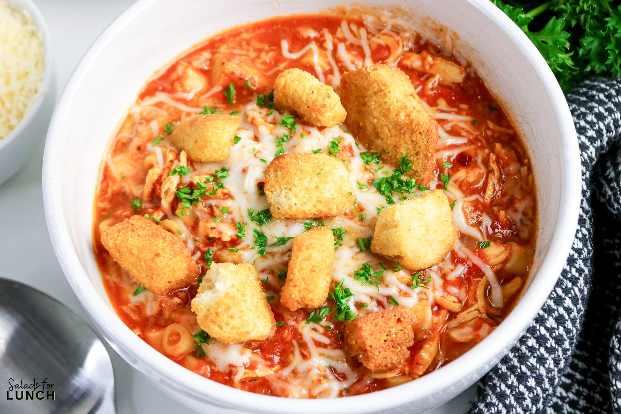 One-Pot Chicken Parmesan Soup - Chicken Parmesan Soup Hero 09 Bowl of tomato-based chicken parm soup topped with melted mozzarella, parsley, and homemade croutons.