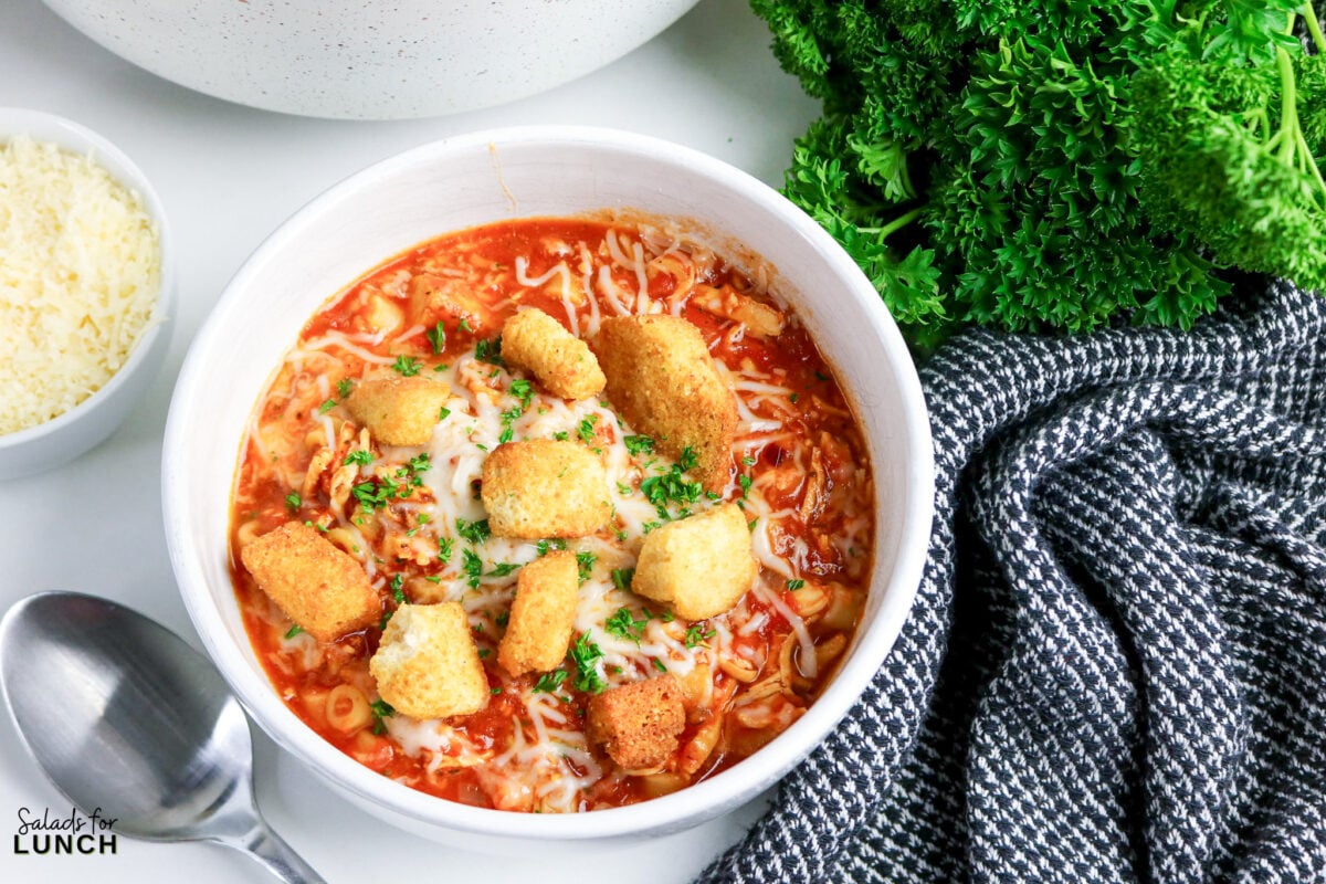 One-Pot Chicken Parmesan Soup - Chicken Parmesan Soup Hero 10 Bowl of tomato-based chicken soup with pasta, melted mozzarella, homemade croutons, and chopped parsley, served with grated parmesan on the side.