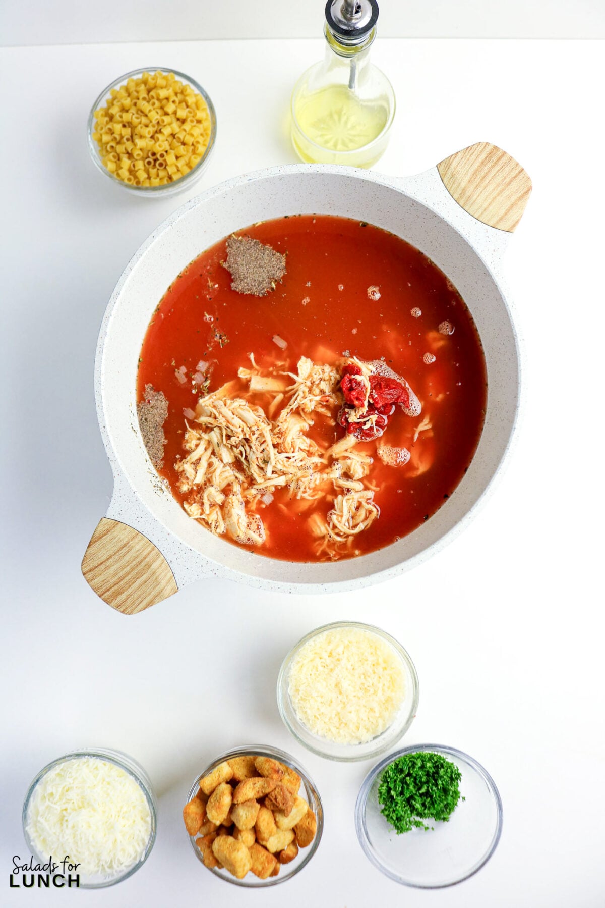One-Pot Chicken Parmesan Soup - Chicken Parmesan Soup Process 10 Pot of tomato broth with shredded chicken, seasonings, and tomato paste, surrounded by bowls of pasta, olive oil, shredded cheese, croutons, and chopped parsley.