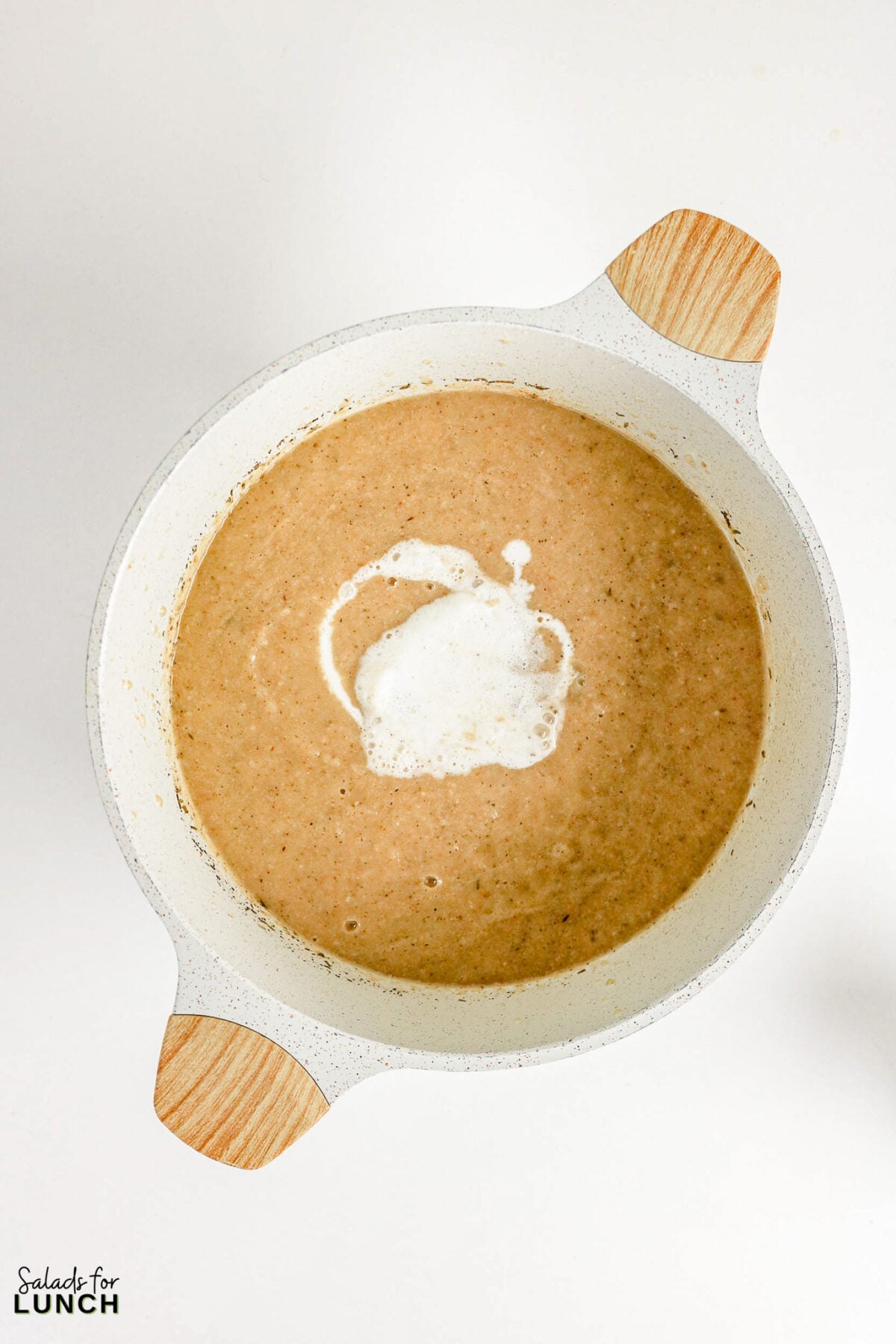 Pureed soup in a pot with a swirl of cream poured on top, viewed from above.
