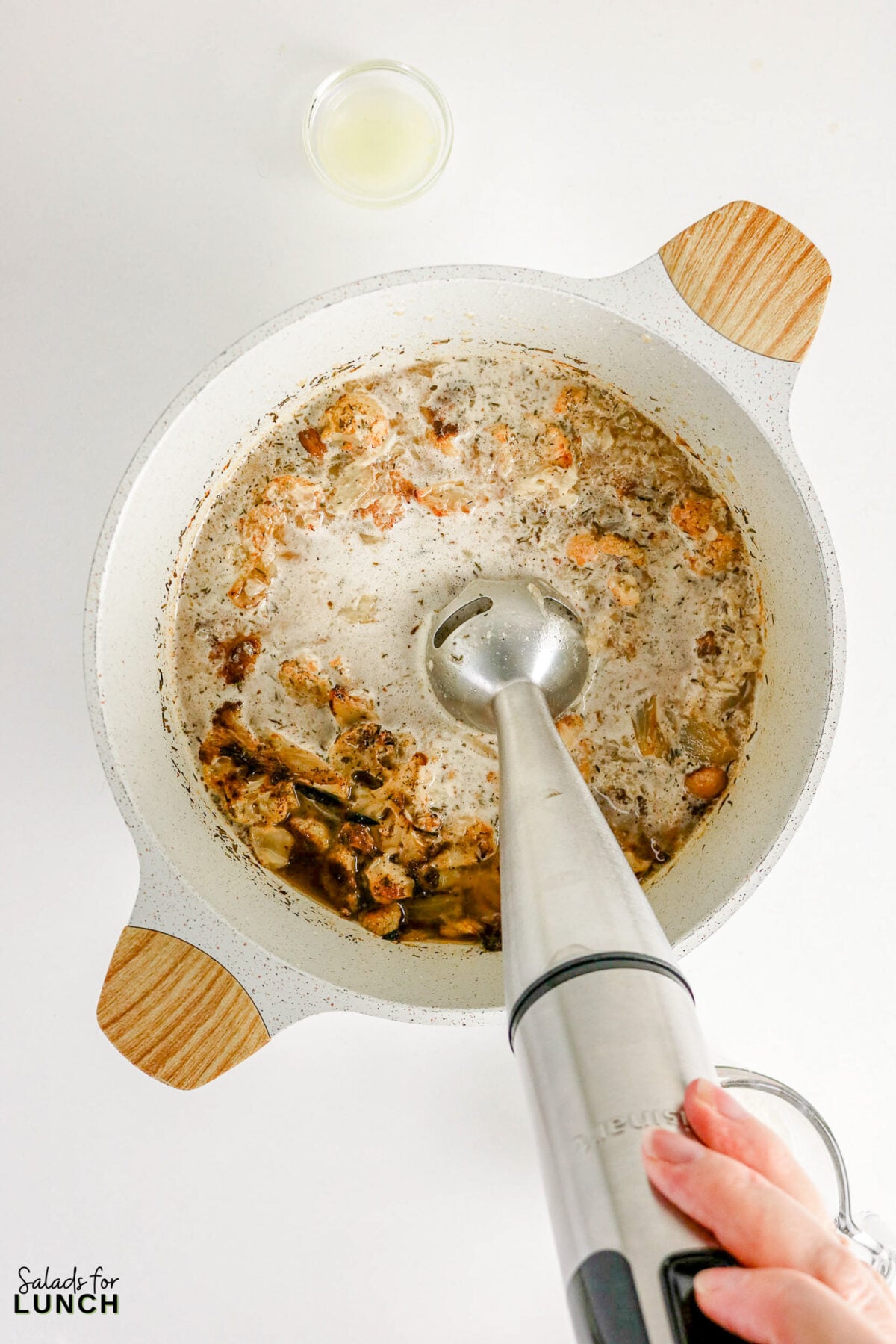 Immersion blender pureeing roasted cauliflower and broth in a pot to make creamy cauliflower soup.