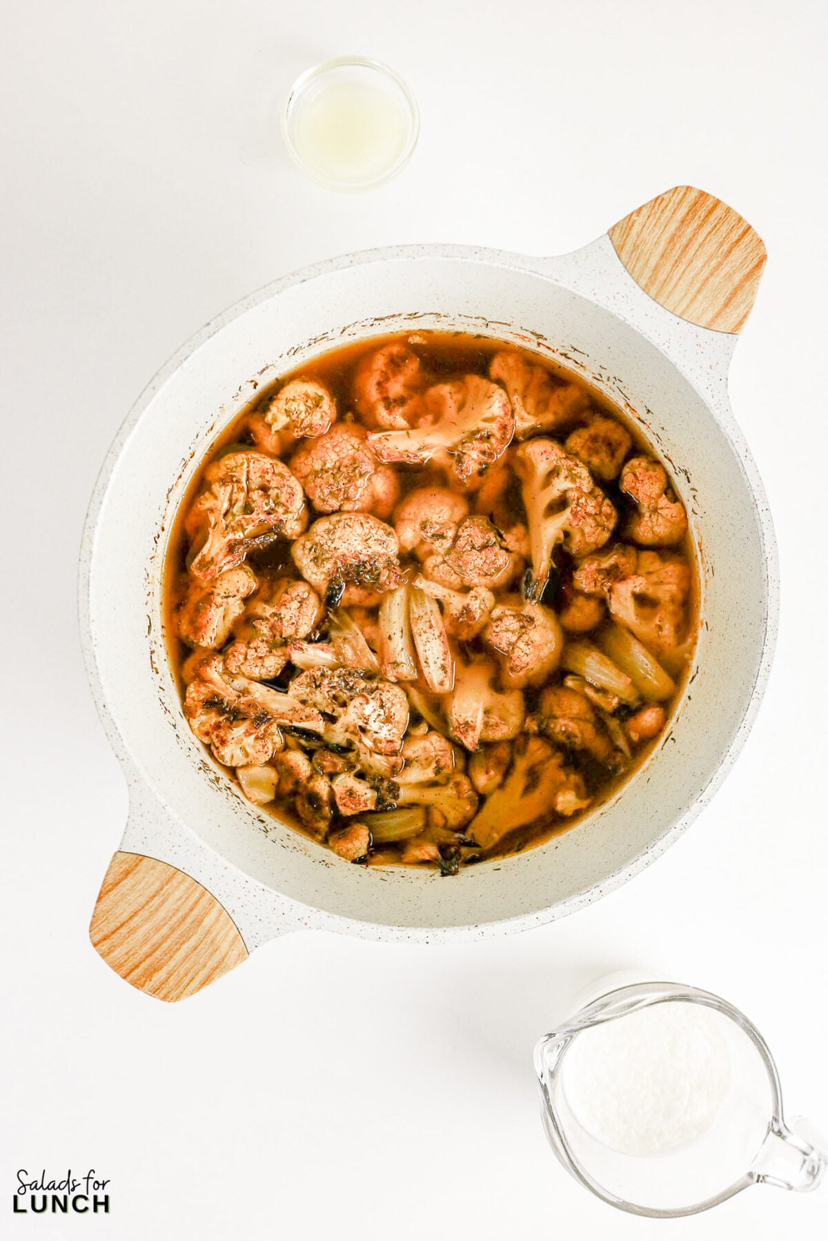 Cauliflower florets simmering in seasoned broth in a pot, with lemon juice and cream on the side.