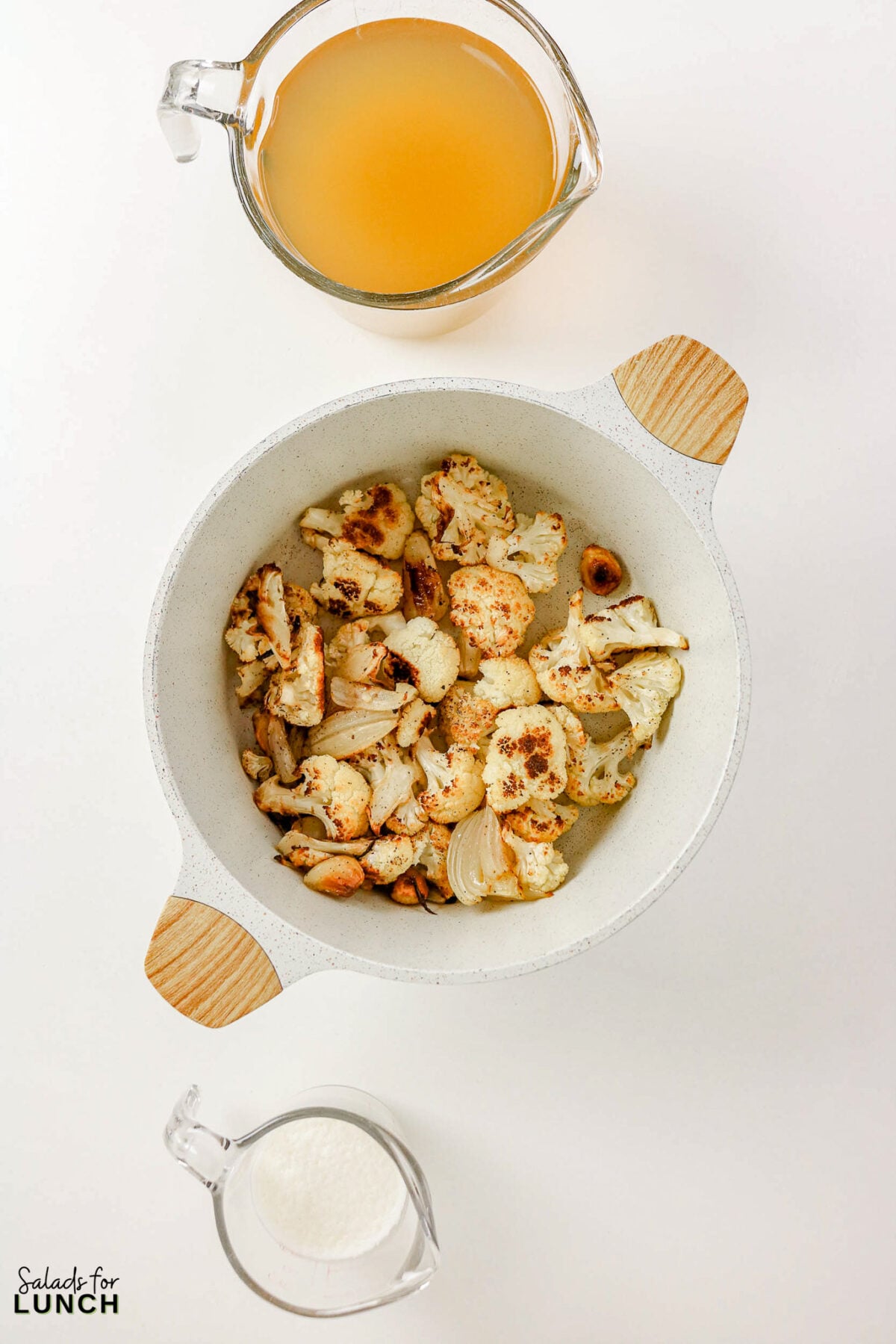 Roasted cauliflower and shallots in a bowl, with broth and cream in glass measuring cups nearby.