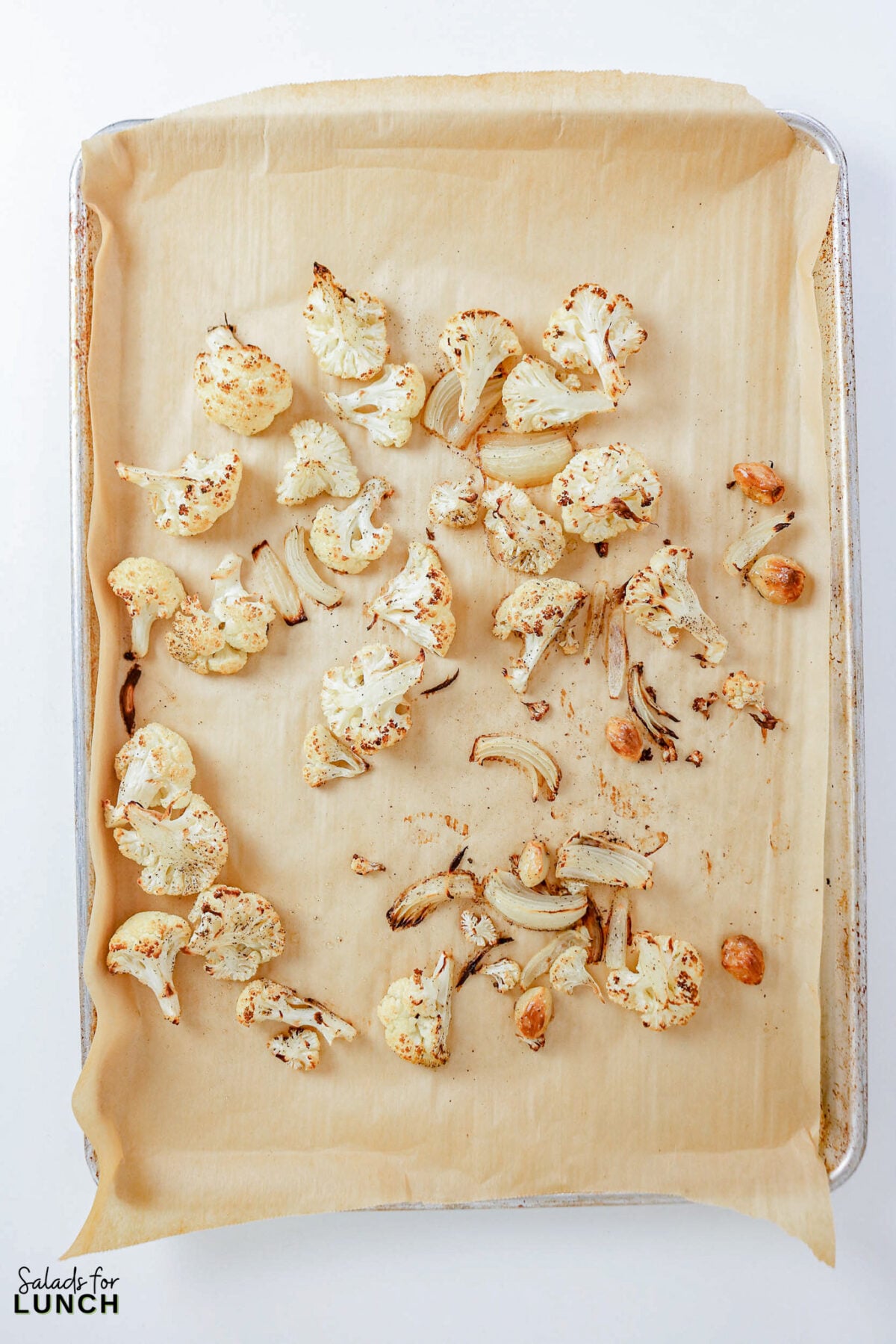 Roasted cauliflower, onion, and garlic cloves golden and caramelized on a parchment-lined baking sheet.