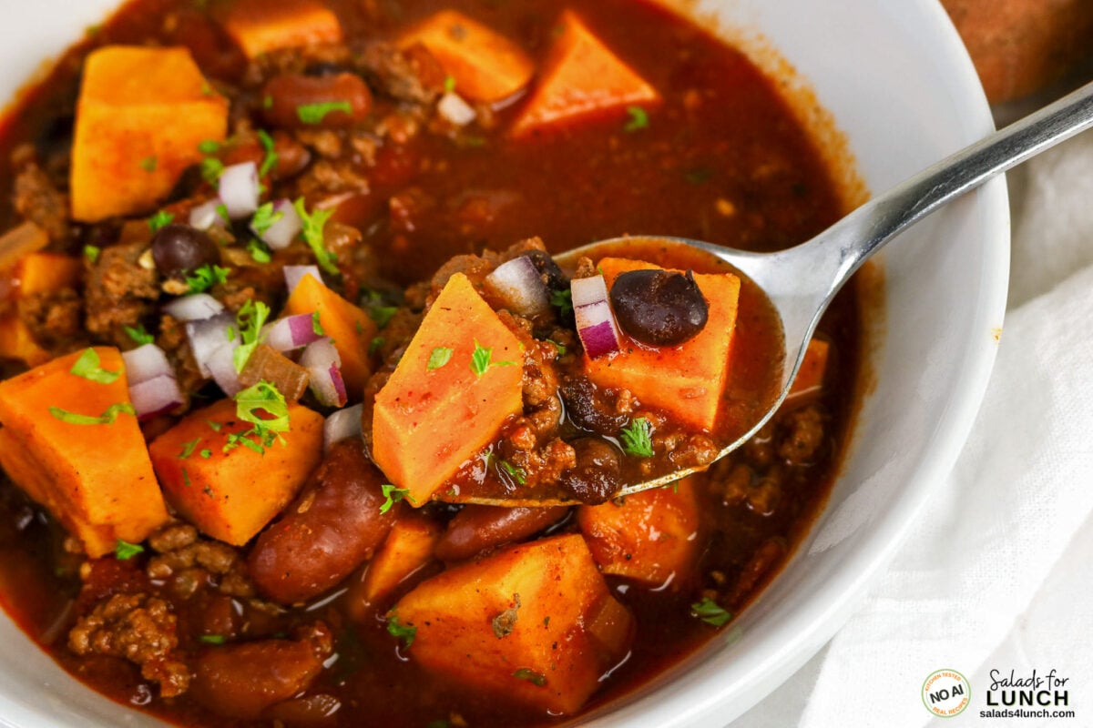 Healthy Sweet Potato Chili with Ground Beef - Sweet Potato Chili Hero 04 Bowl of chili with sweet potato chunks, ground beef, kidney and black beans, topped with red onion and cilantro.