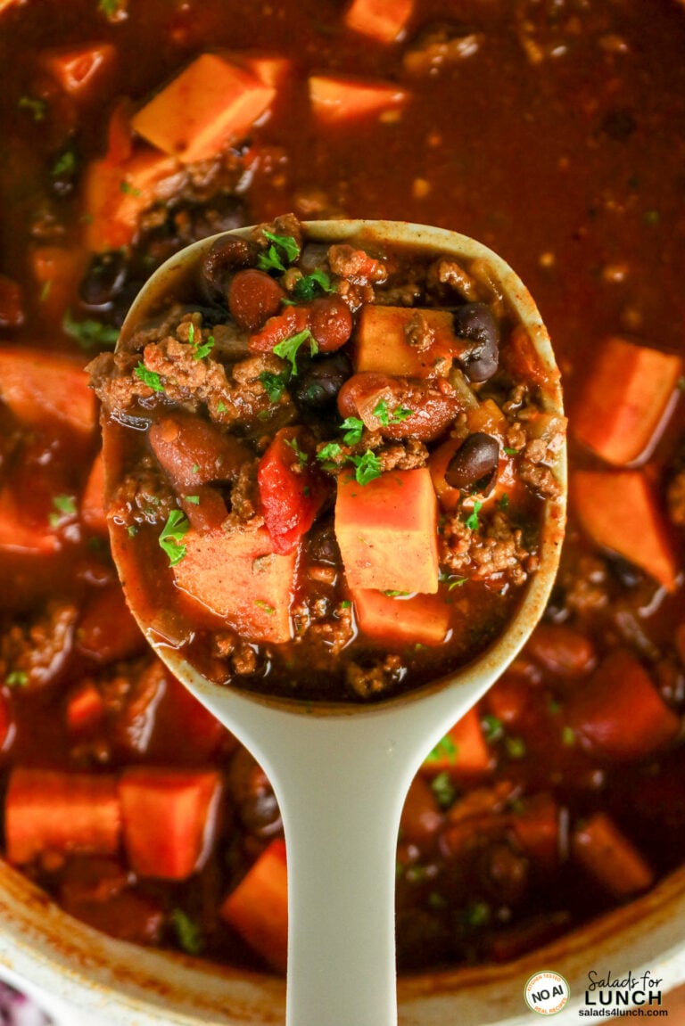 Spoonful of healthy sweet potato chili with ground beef, black beans, kidney beans, sweet potato chunks, and fresh parsley, lifted from a simmering pot.