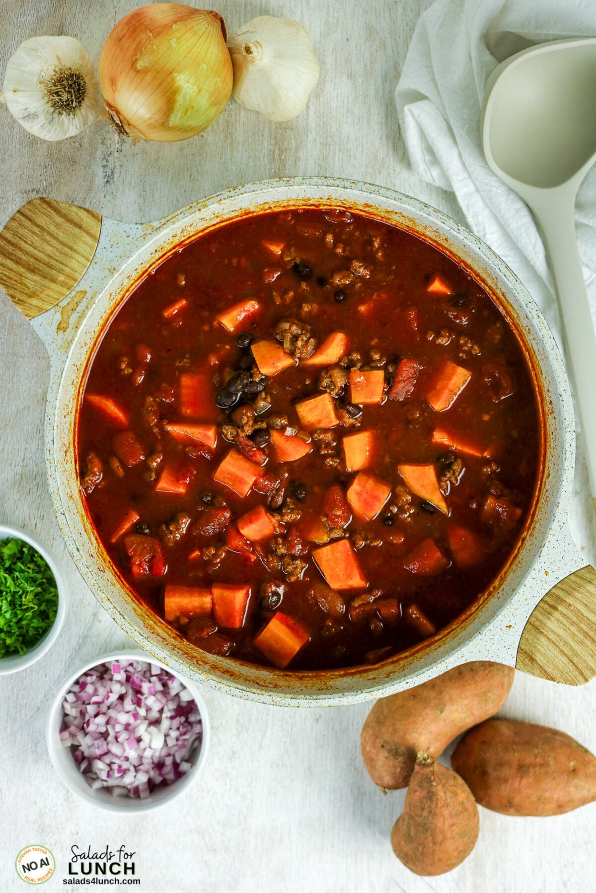 Healthy Sweet Potato Chili with Ground Beef - Sweet Potato Chili Process 01 Pot of simmering sweet potato chili with ground beef and black beans, surrounded by sweet potatoes, onions, garlic and toppings.