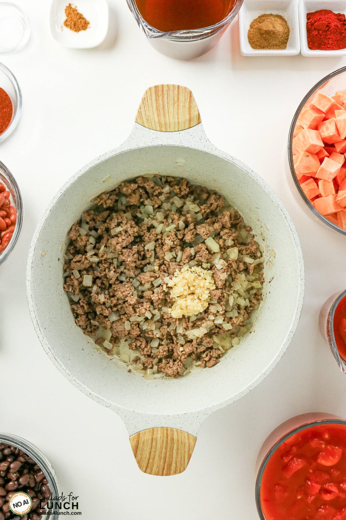 Healthy Sweet Potato Chili with Ground Beef - Sweet Potato Chili Process 10 Browned ground beef and onion in a pot with minced garlic added, surrounded by bowls of diced sweet potatoes, beans, tomatoes and spices.