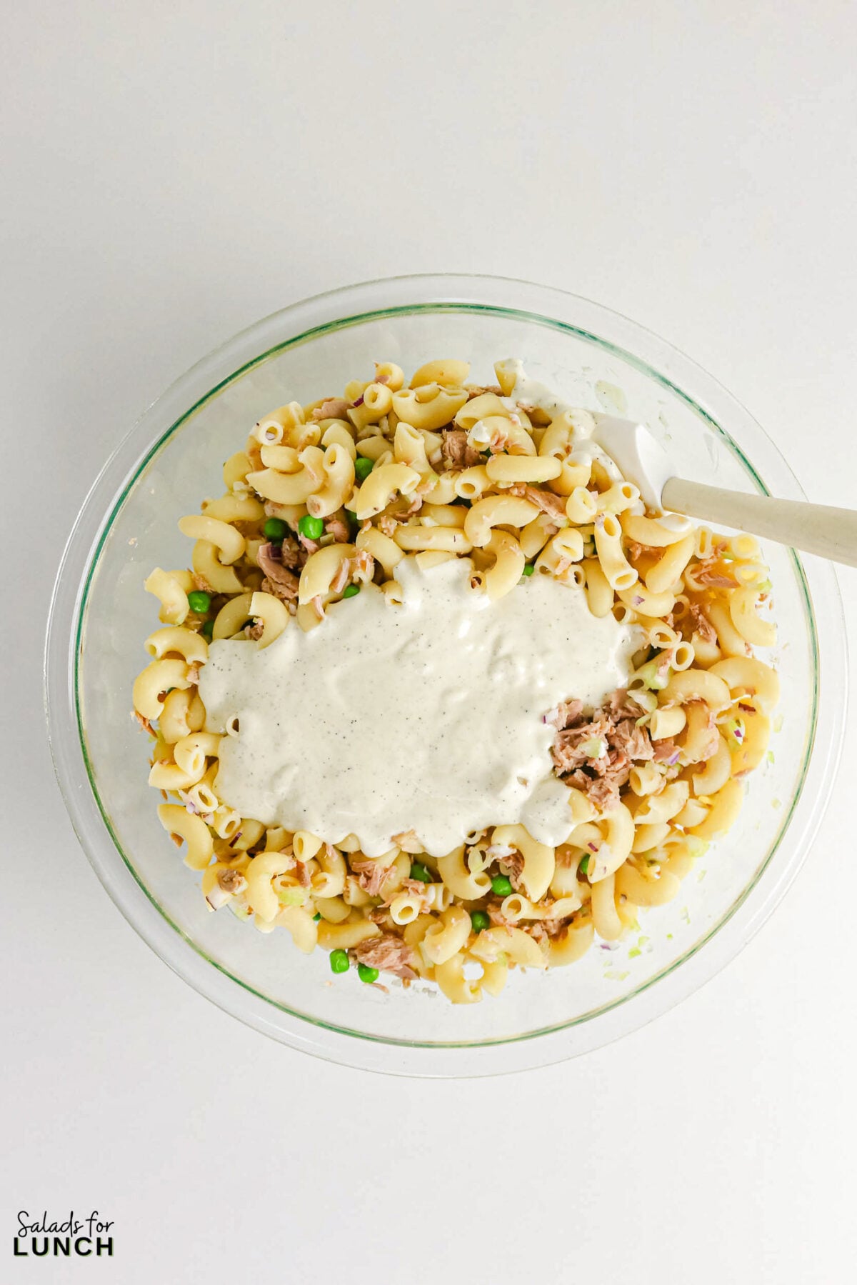 Creamy Tuna Macaroni Salad - Tuna Macaroni Salad Process 3 Creamy dressing being poured over macaroni, tuna, peas and red onion in a glass bowl before mixing.