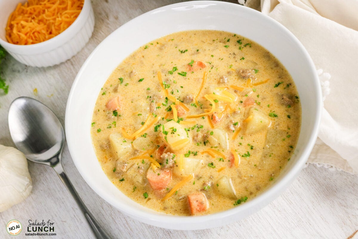 Easy Cheeseburger Soup Recipe - Cheeseburger Soup Recipe Hero 08 Bowl of creamy cheeseburger soup with ground beef, potatoes, carrots, shredded cheddar, and parsley.