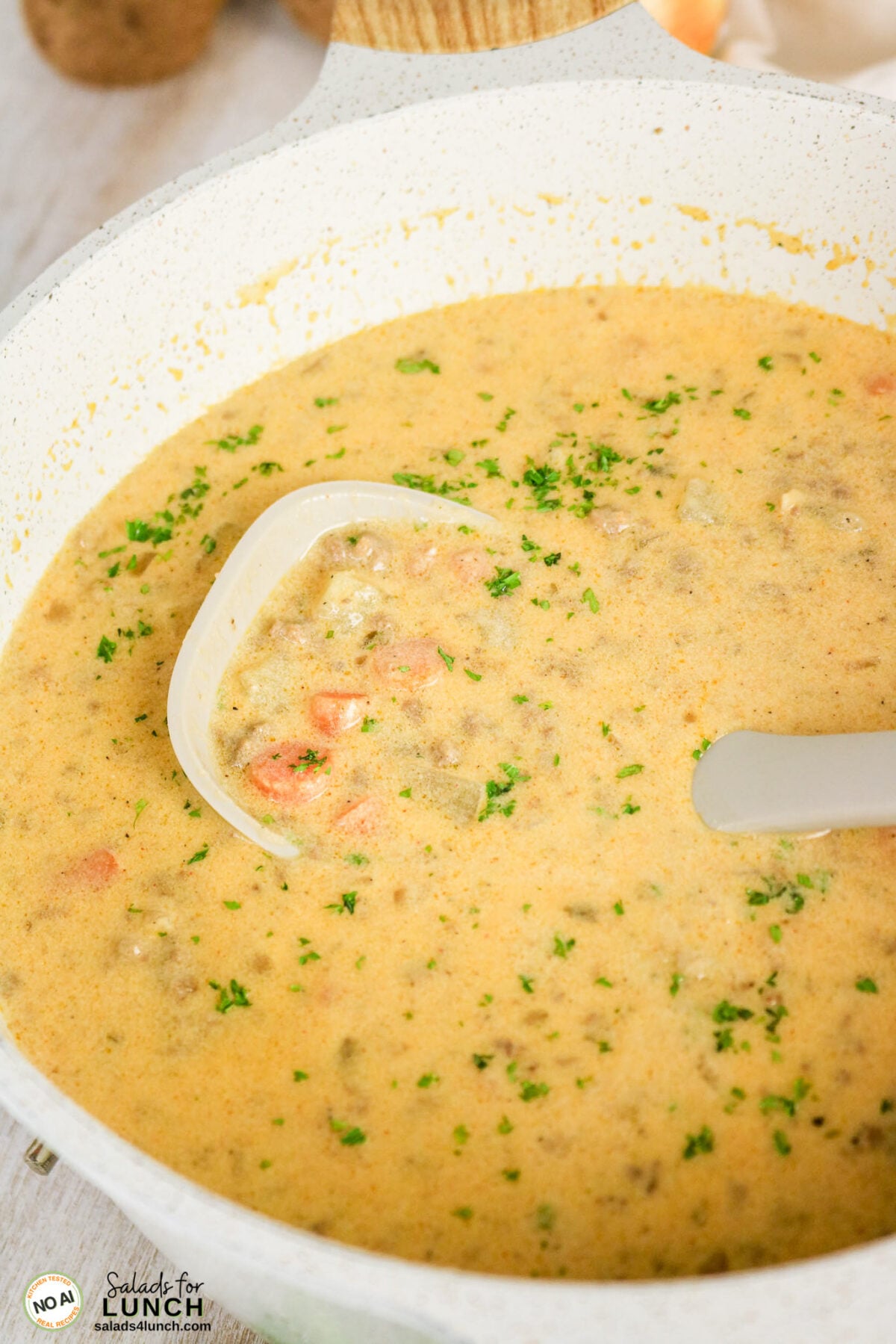 Easy Cheeseburger Soup Recipe - Cheeseburger Soup Recipe Hero 15 Creamy cheeseburger soup with ground meat, diced carrots, and parsley in a pot, ladle scooping a portion.