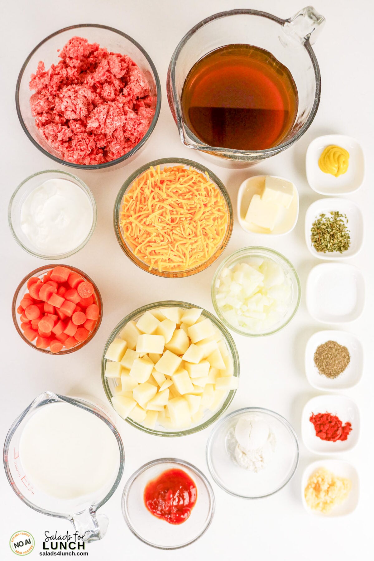 Easy Cheeseburger Soup Recipe - Cheeseburger Soup Recipe Ingredients Overhead view of cheeseburger soup recipe ingredients in bowls: ground beef, broth, shredded cheddar, diced potatoes, carrots, onion, sour cream, milk, ketchup, flour, butter, mustard, dried herbs, pepper, paprika, and minced garlic.