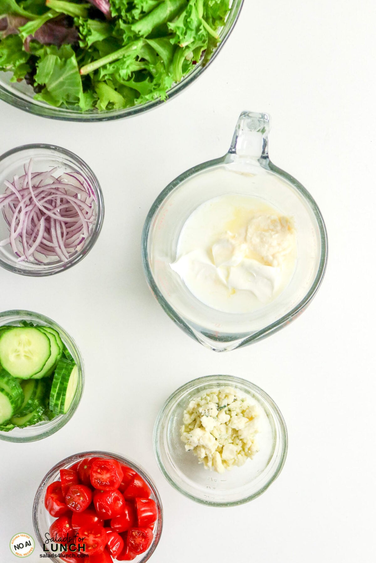 Homemade Blue Cheese Dressing - Homemade Blue Cheese Dressing 2 Salad ingredients arranged in bowls: mixed greens, sliced red onion, cucumber, cherry tomatoes, crumbled blue cheese, and a creamy dressing mixture.