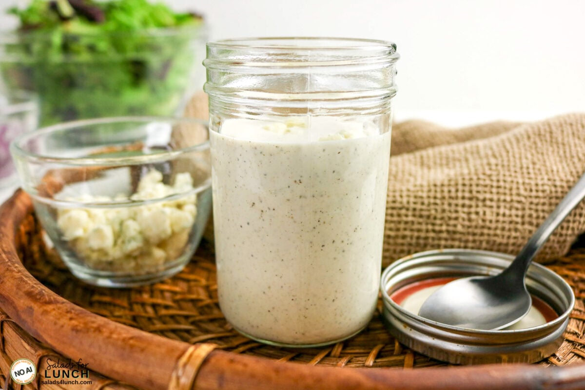 Homemade Blue Cheese Dressing - Steak Salad Bluecheese Dressing 07 Creamy blue cheese dressing in a mason jar with a bowl of crumbled blue cheese and salad greens nearby.