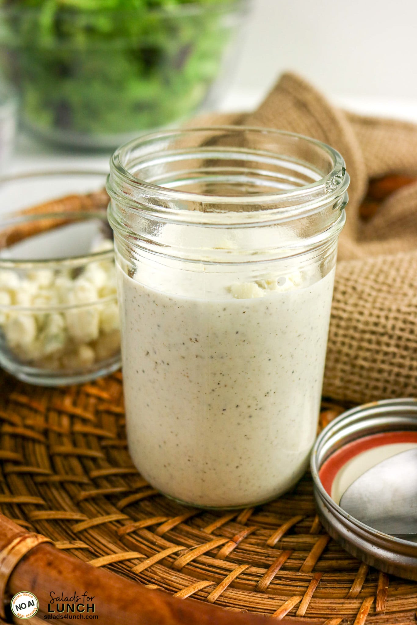 Creamy homemade blue cheese dressing in an open mason jar, with crumbled cheese and salad greens in the background.