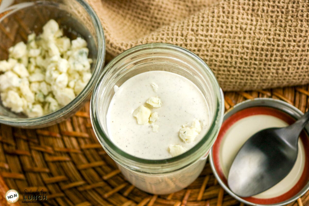 Homemade Blue Cheese Dressing - Steak Salad Bluecheese Dressing 11 Jar of creamy blue cheese dressing topped with crumbles on top, next to a bowl of more blue cheese crumbles.