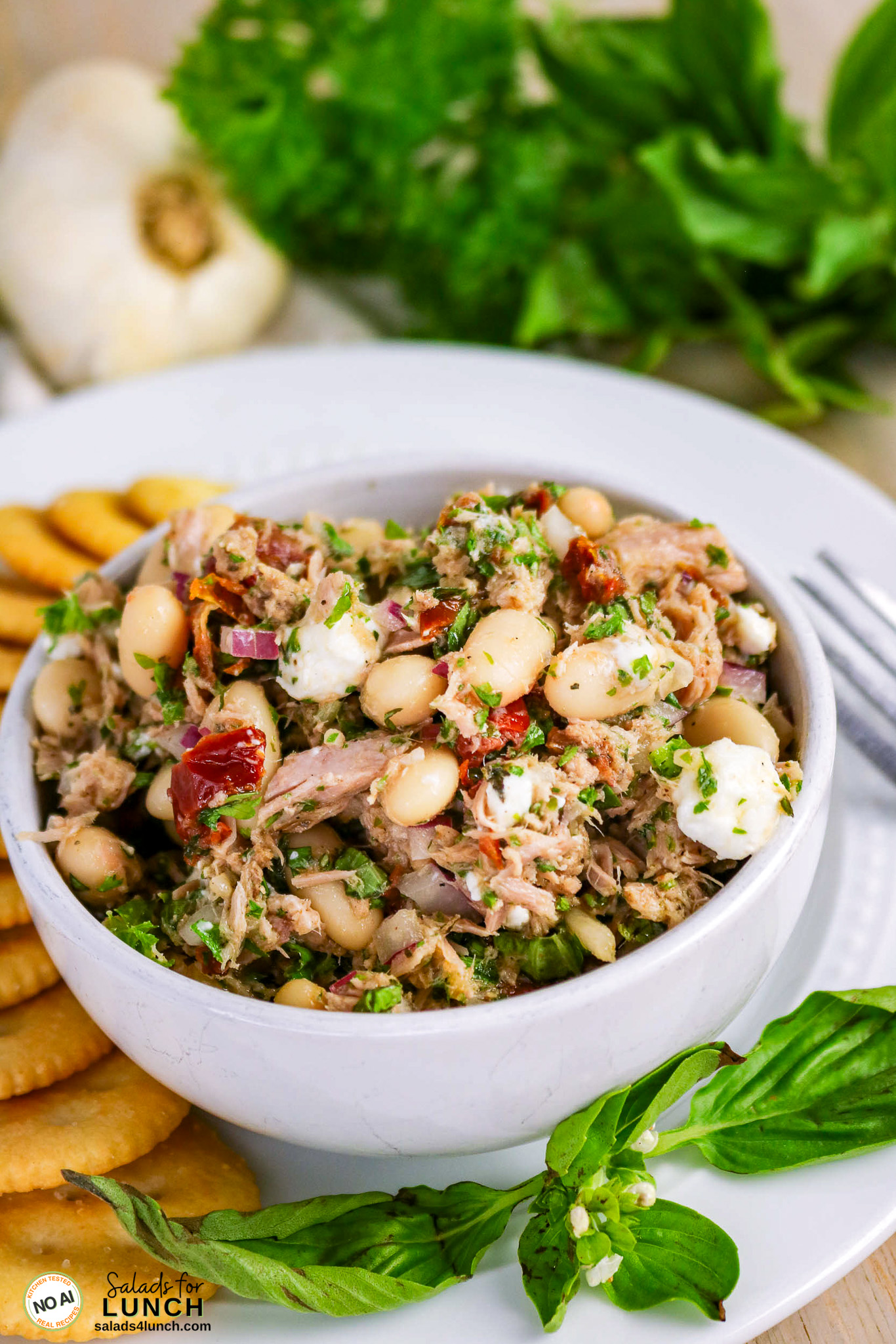Bowl of Tuscan Tuna Salad bean with cannellini beans, sun-dried tomatoes, red onion, feta, and herbs, served with crackers.