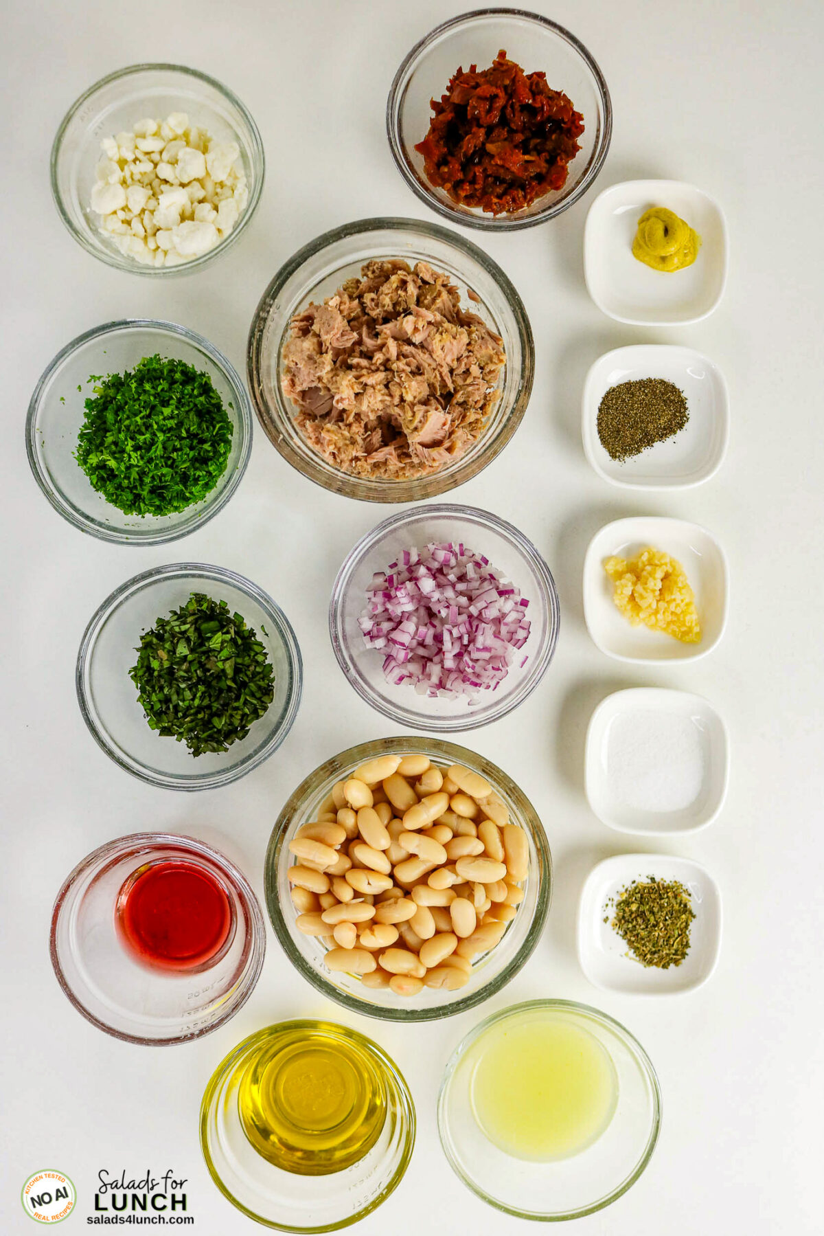 Tuscan Tuna Salad - Tuscan Tuna Salad Ingredients Tuna white bean and tuna salad ingredients in bowls: feta, sun-dried tomatoes, tuna, parsley, basil, red onion, white beans, garlic, mustard, pepper, salt, oregano, vinegar, olive oil, lemon juice.