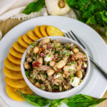 Bowl of tuscan tuna and white bean salad with sun-dried tomatoes, feta, and herbs, served with round crackers.