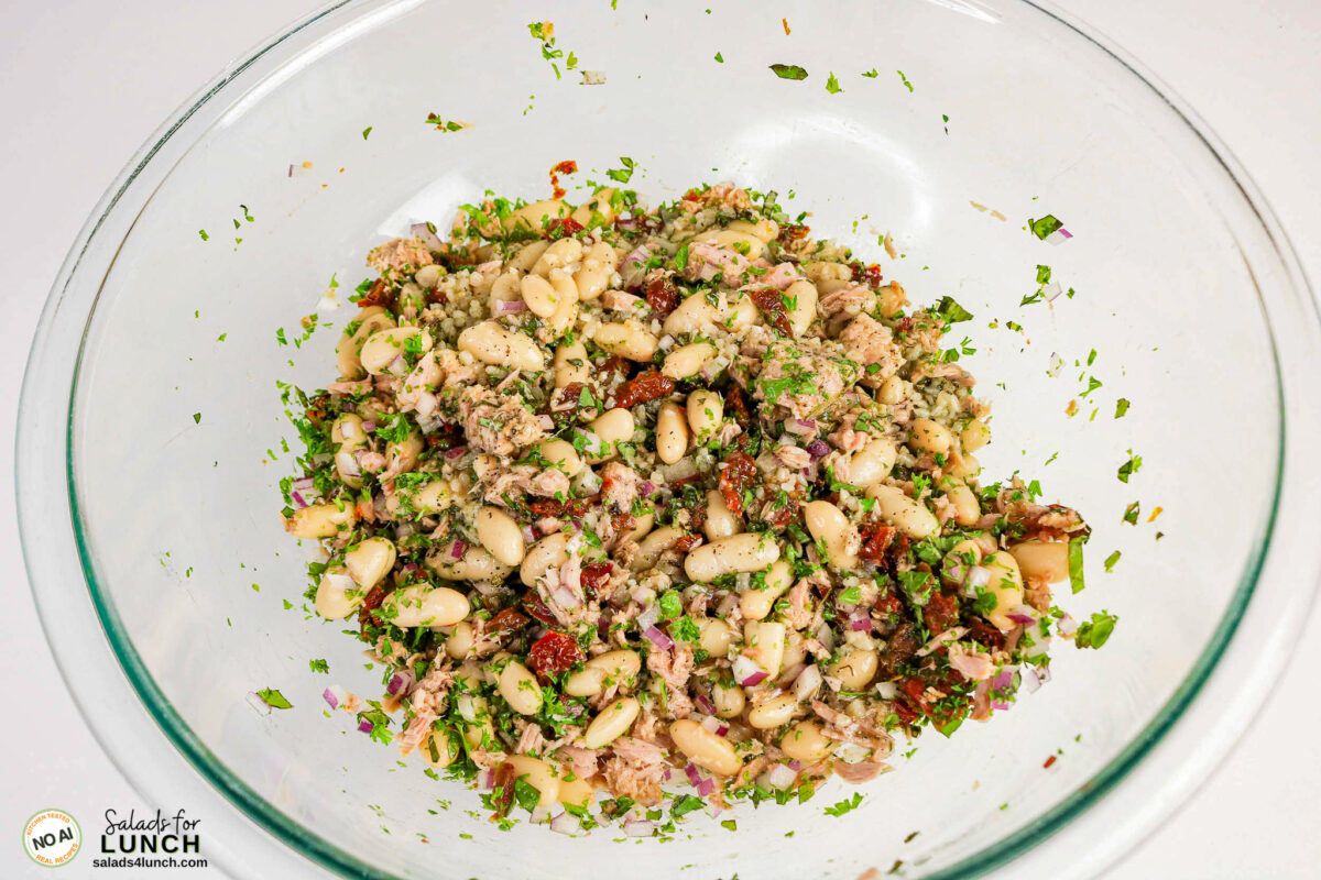 Tuscan Tuna Salad - Tuscan Tuna Salad Process 07 White bean and tuna salad with chopped parsley, red onion, and sun-dried tomatoes in a glass bowl.